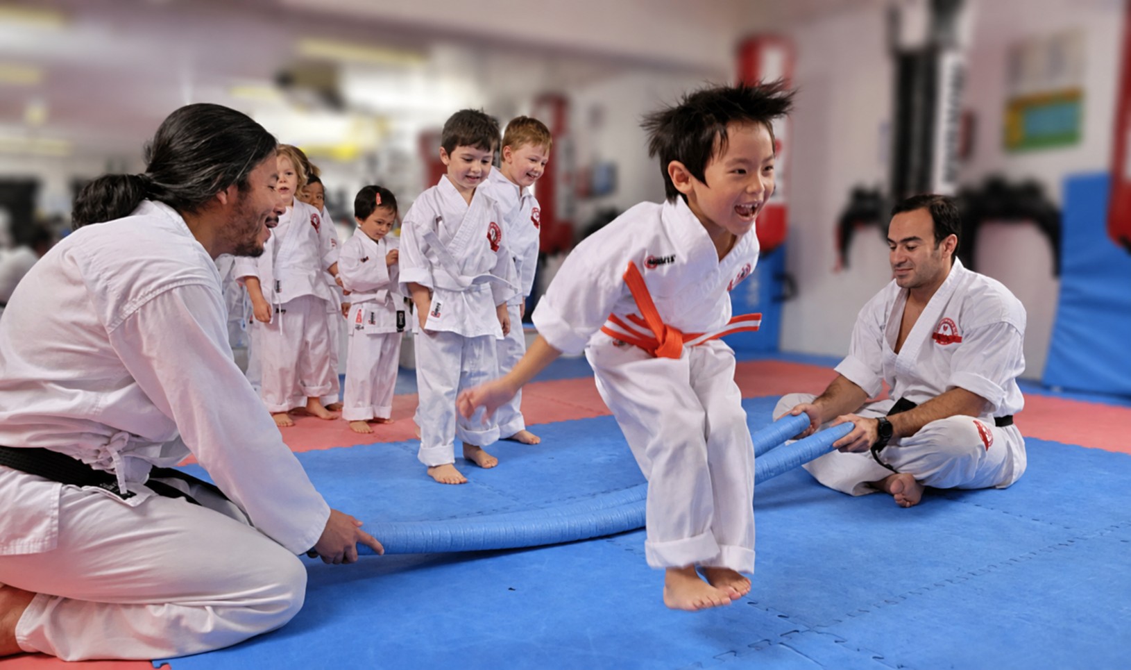 Young BX1 Kids Karate student smiling while jumping over a training obstacle in class