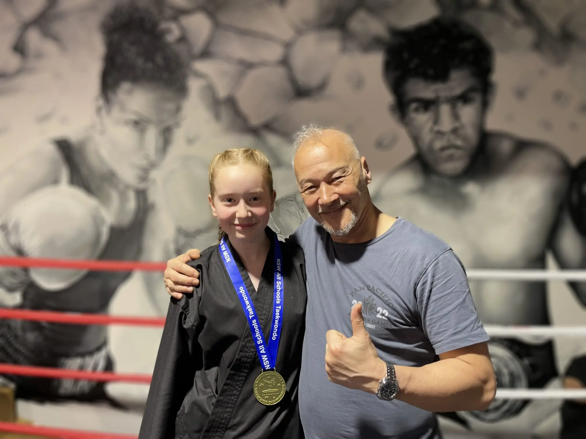 BX1 junior martial arts student celebrating a medal with her coach in Neutral Bay